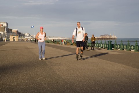 ENGLAND, East Sussex, Brighton, Woman jogging with man rollerblading on the seafront promenade.