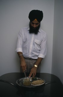 ENGLAND, Religion, Sikhism, Sikh man using short knife or kirpan to bless food.