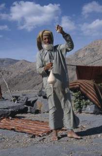UAE, Oman, Jabal Shams, Elderly man using spindle to spin thread for rug making.