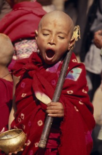 NEPAL, Kathmandu Valley, Bhaktapur, Young monk yawning during a ceremony and wearing red robes