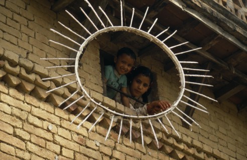 NEPAL, Kathmandu Valley, Children looking out of a window framed by the sun symbol of the Communist