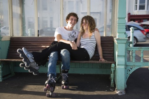 ENGLAND, East Sussex, Brighton, "Young couple sat on bench on the seafront promenade. One wearing