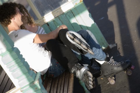 ENGLAND, East Sussex, Brighton, "Young couple sat on bench on the seafront promenade. One wearing