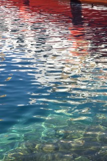 SPAIN, Canary  Islands, Lanzarote, Red and white reflection of boat in rippled water of harbour