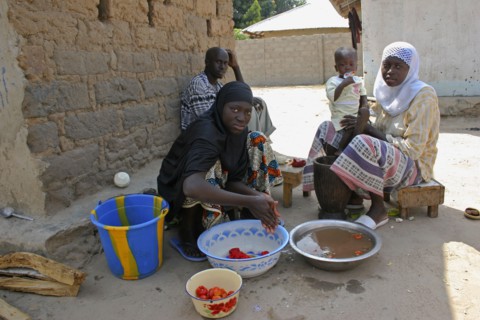GAMBIA, Western Gambia, Tanji, Man sitting in shade in yard outside his house in the company of two