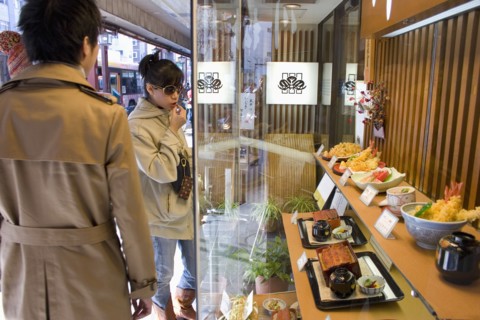 JAPAN, Honshu, Tokyo, Asakusa.  Young Japanese couple standing outside a restaurant looking at the