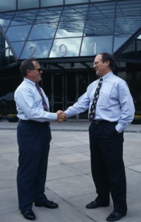 USA, Florida, Orlando, Two businessmen in conversation shaking hands outside modern glass fronted
