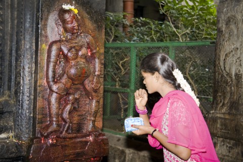 INDIA, Tamil Nadu, Madurai, "Young woman standing beside shrine depicting Goddess of Fertility,