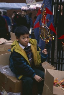 ENGLAND, London, Chinese New Year, Young boy sitting on boxes holding up decoration for New Year