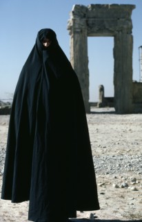 IRAN, Fars Province , Persepolis, Full length standing portrait of a woman wearing a black Chador