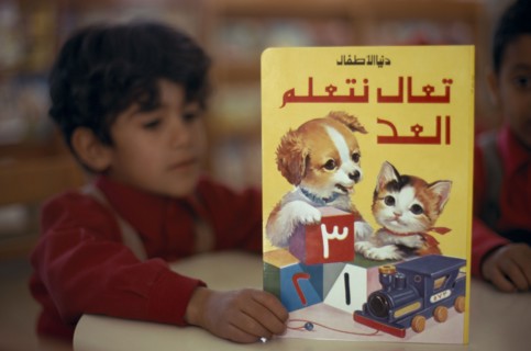 KUWAIT, Education, School boy reading a colourful book illustrated with a kitten and puppy