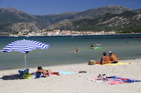 FRANCE, Corsica, St Florent, Bathers & sandy beach with St Florent old town in distance