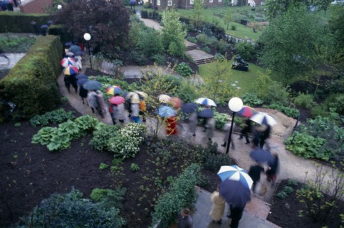 ENGLAND, East Sussex, Glyndebourne, Opera attendees walking through the gardens holding umbrellas