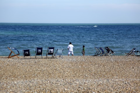 ENGLAND, East Sussex, Eastbourne, Man and young boy on the beach with deck chairs blowing in the