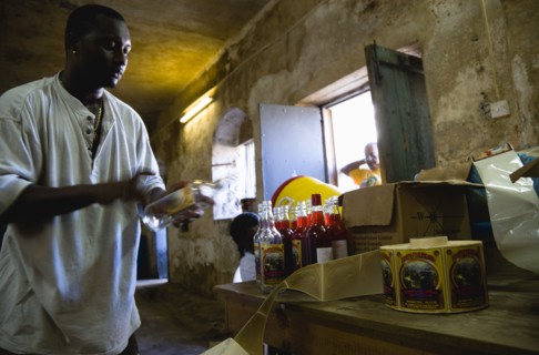 WEST INDIES, Grenada, St Patrick, Male worker hand labelling the bottles at the River Antoine rum