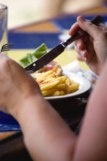WEST INDIES, Grenada, St George, Sunburnt white caucasian woman eating a plate of potato chips and