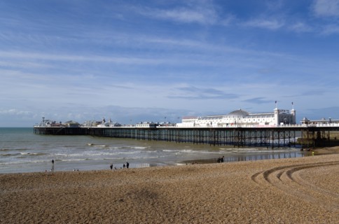ENGLAND, East Sussex, Brighton, The Pier at low tide with people on the shingle pebble beach.