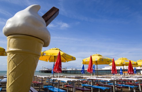 ENGLAND, East Sussex, Brighton, The Pier at low tide with shingle pebble beach and sunshade