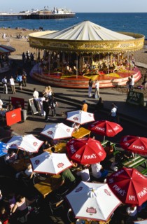 ENGLAND, East Sussex, Brighton, People sitting under sun shade umbrellas at tables on the promenade