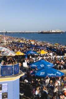 ENGLAND, East Sussex, Brighton, People sitting under sun shade umbrellas at tables on the promenade