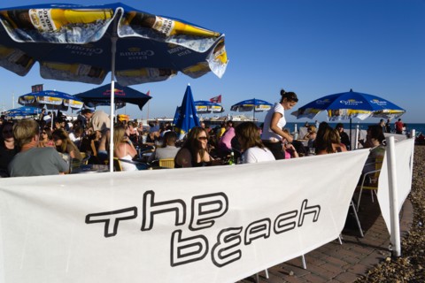 ENGLAND, East Sussex, Brighton, People sitting under sun shade umbrellas at tables on the promenade