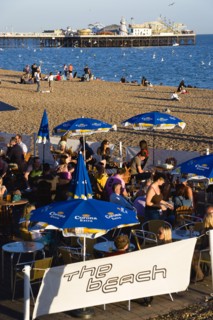 ENGLAND, East Sussex, Brighton, People sitting under sun shade umbrellas at tables on the promenade