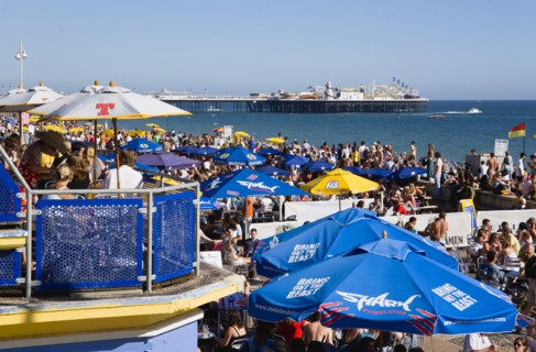ENGLAND, East Sussex, Brighton, People sitting under sun shade umbrellas at tables on the promenade