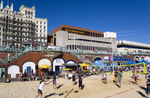 ENGLAND, East Sussex, Brighton, Young people playing beach volleyball on sand on the seafront with