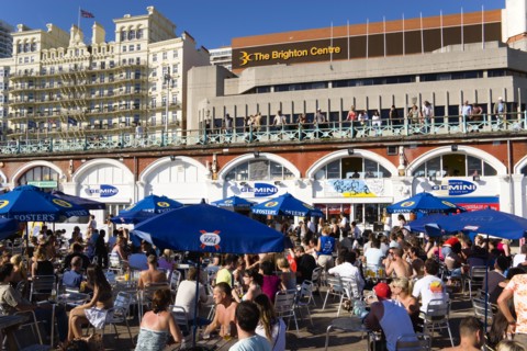 ENGLAND, East Sussex, Brighton, People sitting under sun shade umbrellas at tables on the promenade