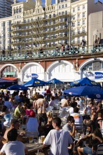 ENGLAND, East Sussex, Brighton, People sitting under sun shade umbrellas at tables on the promenade