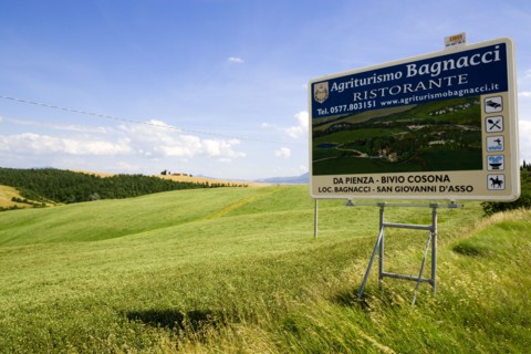 ITALY, Tuscany, Val D'Orcia, Agritourism sign for restaurant in field of ripe crops in the valley