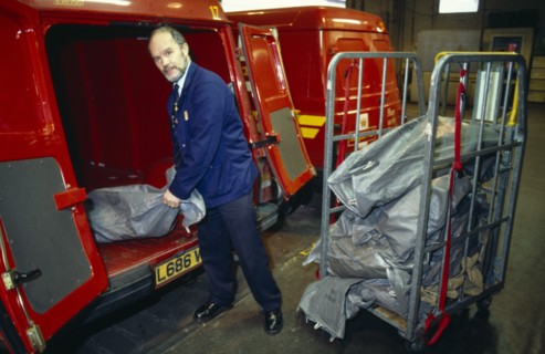 England, East Sussex, Brighton, Male Postal worker unloading sacks of mail from the back of a Post