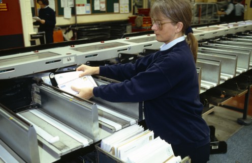 England, East Sussex, Brighton, Female Postal worker collecting sorted mail at the end of the OCR