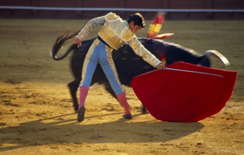 Spain, Andalucia, Seville, matador holding sword behind raised cape in passing move with charging