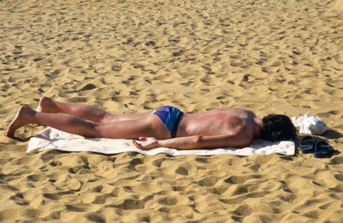 Sri Lanka, Negombo, Single man sunbathing on towel on sand of beach and turning red with sunburn.