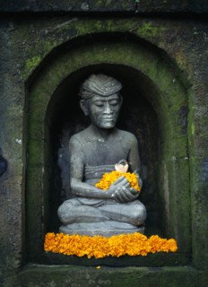 Indonesia, Bali, Ubud, Stone statue of male figure in niche of wall sitting in lotus position
