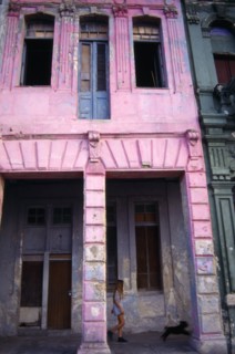 CUBA, Havana, Pink painted crumbling facade of house on the Malecon with girl and dog walking past.