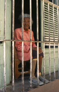 CUBA, Trinidad, Portrait of elderly woman sitting behind barred window.