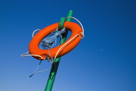IRELAND, County Dublin, Howth, Red life belt on green stand with blue sky and plane behind.