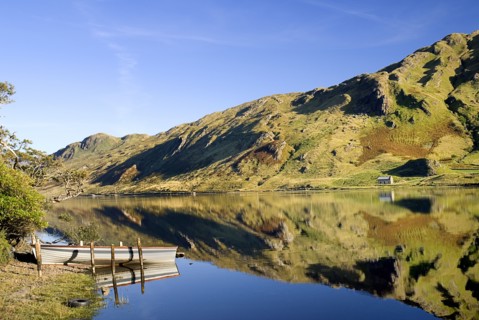 IRELAND, County Galway, Connemara, Kylemore Lough with rowing boat and reflection of stone cottage