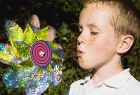 Children, Toys, Outdoors, Young boy blowing toy windmill gently.