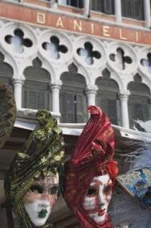 Venice, Veneto, Italy. Red green blue and gold carnival masks in front of partly seen facade of the