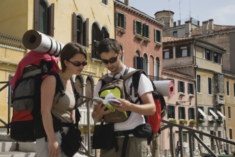 Venice, Veneto, Italy. Two young backpacker tourists wearing sunglasses and carrying rucksacks