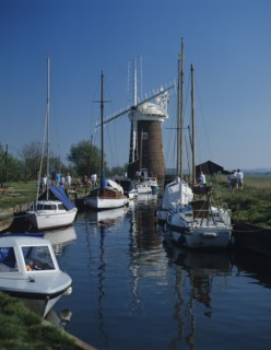 The Norfolk Broads, Norfolk, England. People walking along path next to canal with moored pleasure