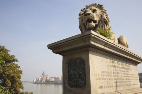 Budapest, Pest County, Hungary. Lion sculpture on the Chain Bridge with Hungarian Parliament