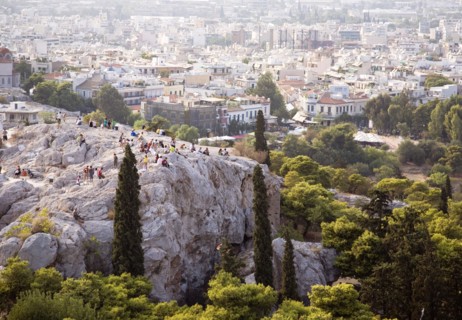 Athens, Attica, Greece. Tourists on rocks below the Acropolis overlooking Odeon of Herodes Atticus
