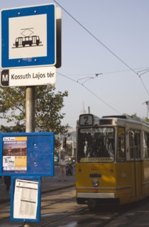 Budapest, Pest County, Hungary. Yellow tram approaching stop and signpost displaying timetable.