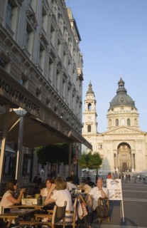 Budapest, Pest County, Hungary. Cafe with Summer tourists seated at outside tables with Saint