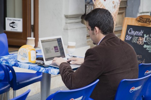 Budapest, Pest County, Hungary. Hungarian man has coffee at outside table while using laptop online
