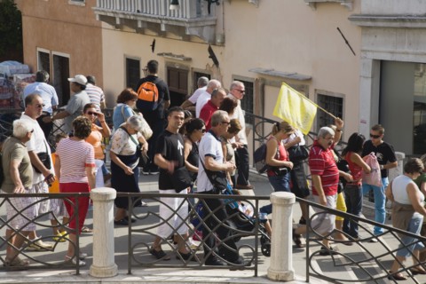 Venice, Veneto, Italy. Tour group of tourists crossing bridge in late summer led by guide holding